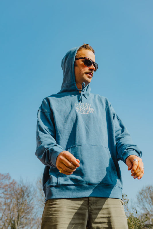 Man wearing a blue hoodie with a logo against a clear blue sky