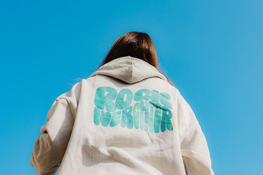 Person wearing a beige jacket with 'Rock My Sister' text on the back against a clear blue sky.