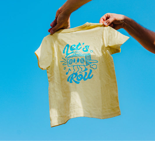 Yellow t-shirt with blue graphic and text held against a clear blue sky
