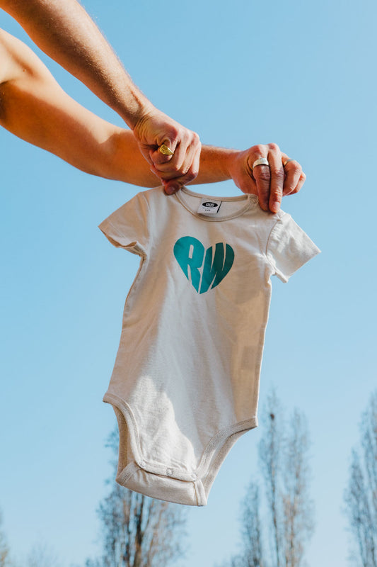 Baby onesie with a green heart logo held against a blue sky