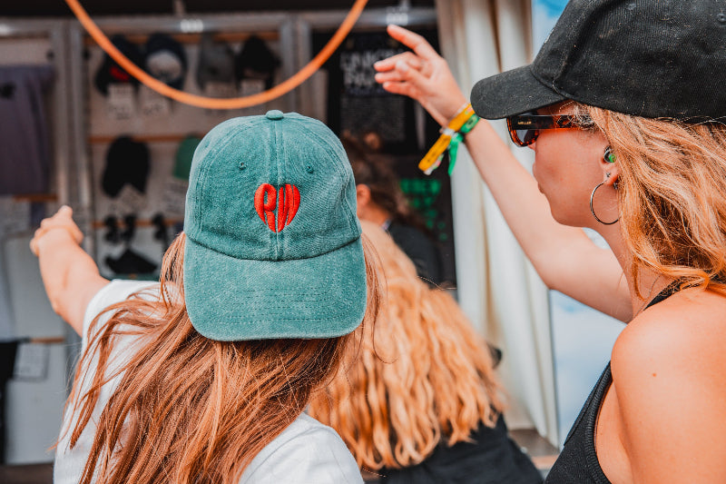 Two people with hats, one green with a red heart design, in an indoor setting.