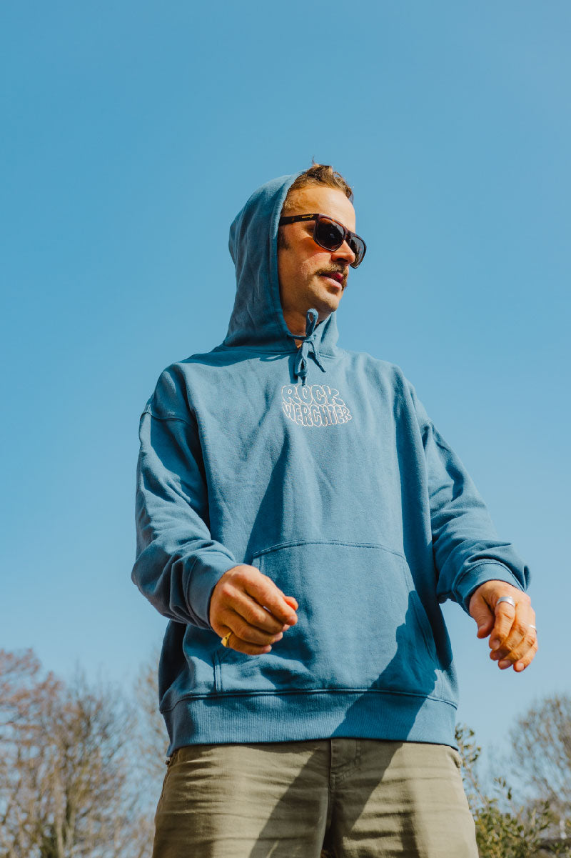 Man wearing a blue hoodie with a logo against a clear blue sky