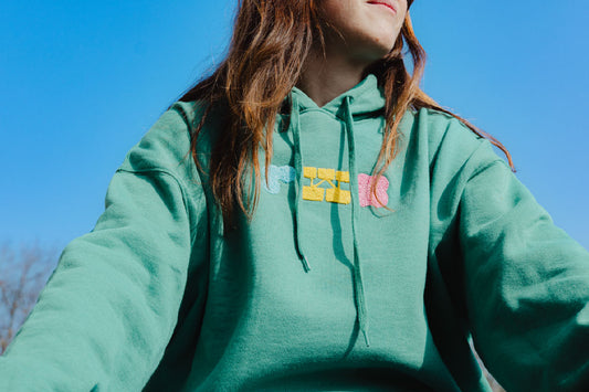 Person wearing a green hoodie with colorful text design against a clear blue sky.
