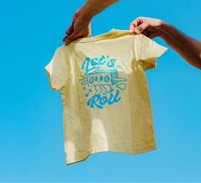 Yellow t-shirt with blue graphic and text held against a clear blue sky