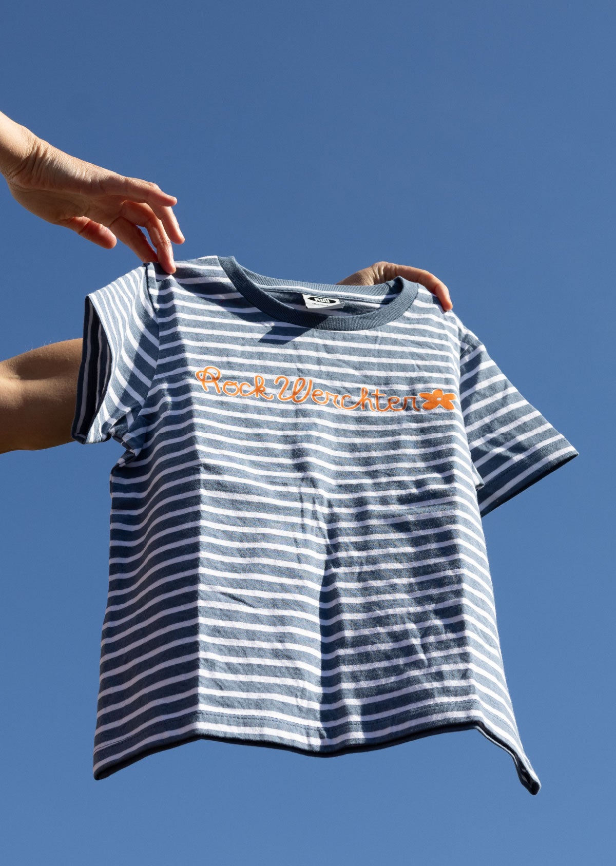 Striped t-shirt with text held against a clear blue sky