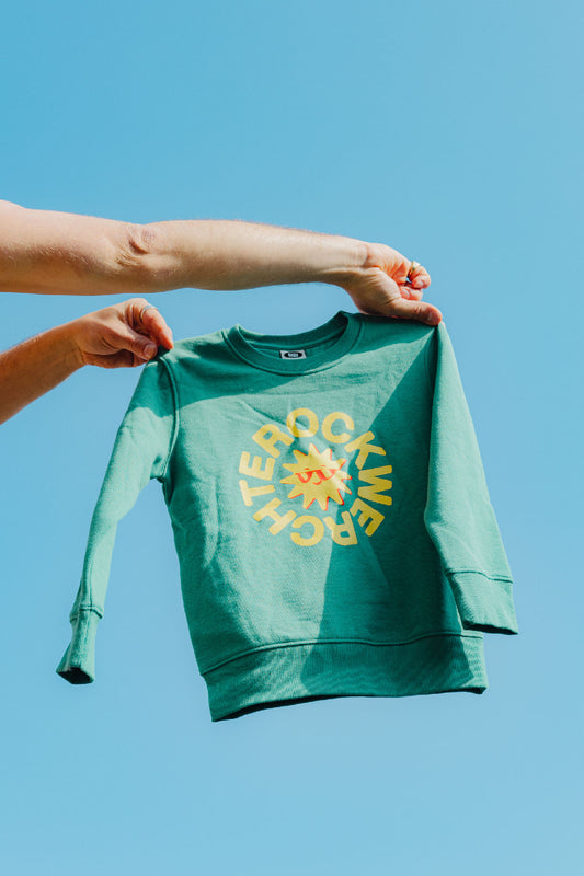 Green sweatshirt with a yellow graphic design held against a clear blue sky