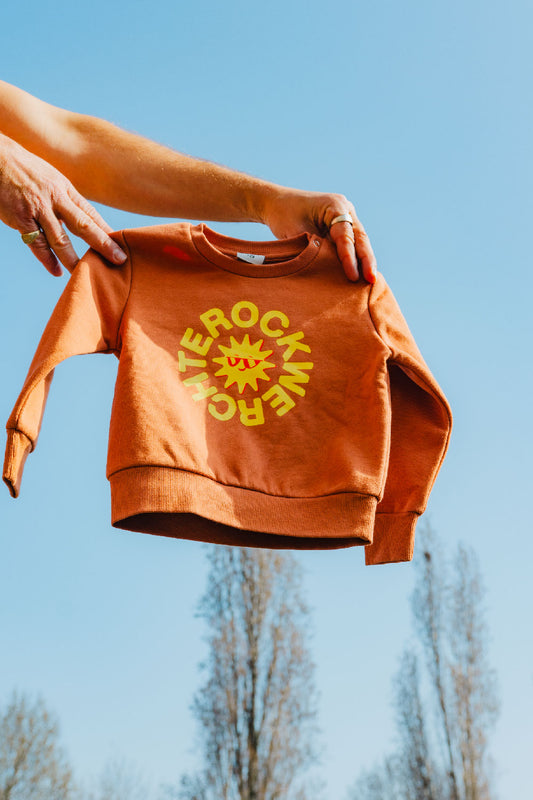 Orange sweatshirt with yellow text held against a blue sky