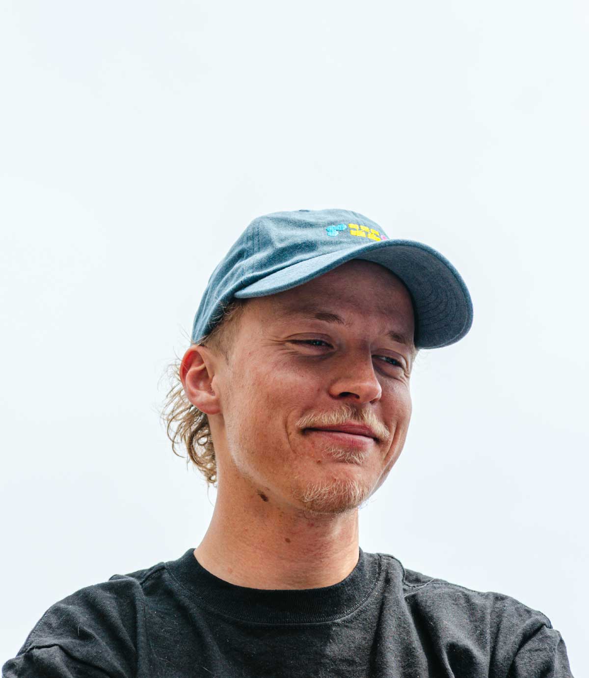 Man wearing a blue cap with a logo on a light gray background