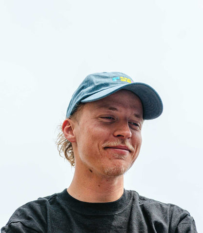 Man wearing a blue cap with a logo on a light gray background