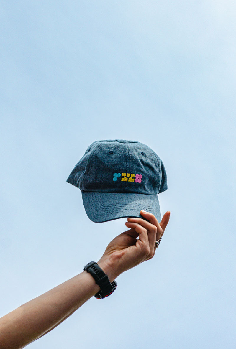 Blue denim cap with colorful text held against a clear blue sky