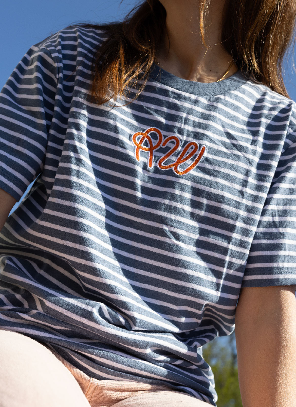 Person wearing a blue and white striped t-shirt with orange text, sitting outdoors.