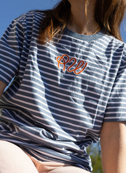 Person wearing a blue and white striped t-shirt with orange text, sitting outdoors.
